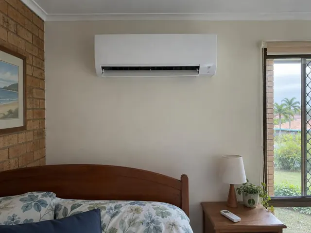 Wall-mounted split system above a bed in a bedroom with brick and painted walls in Bundall