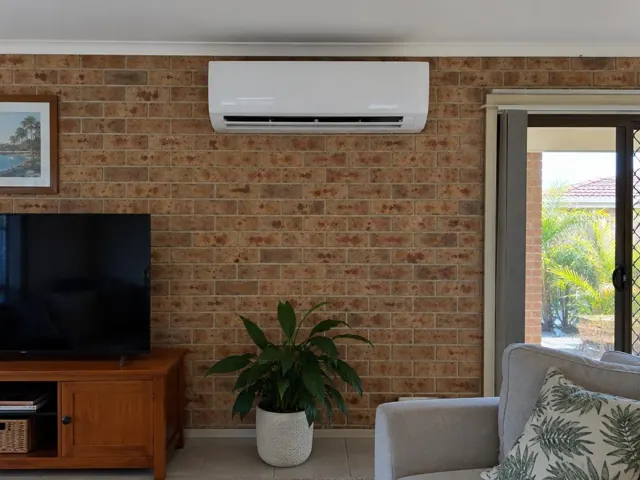 Wall-mounted split system on a brick feature wall in a living room with sliding door in Broadbeach Waters